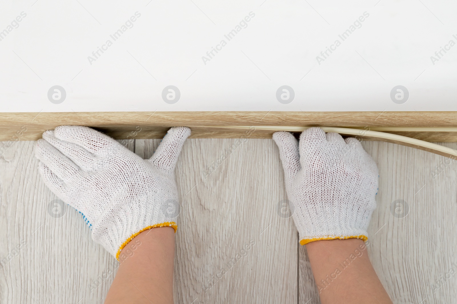 Photo of Man installing plinth on laminated floor in room, top view