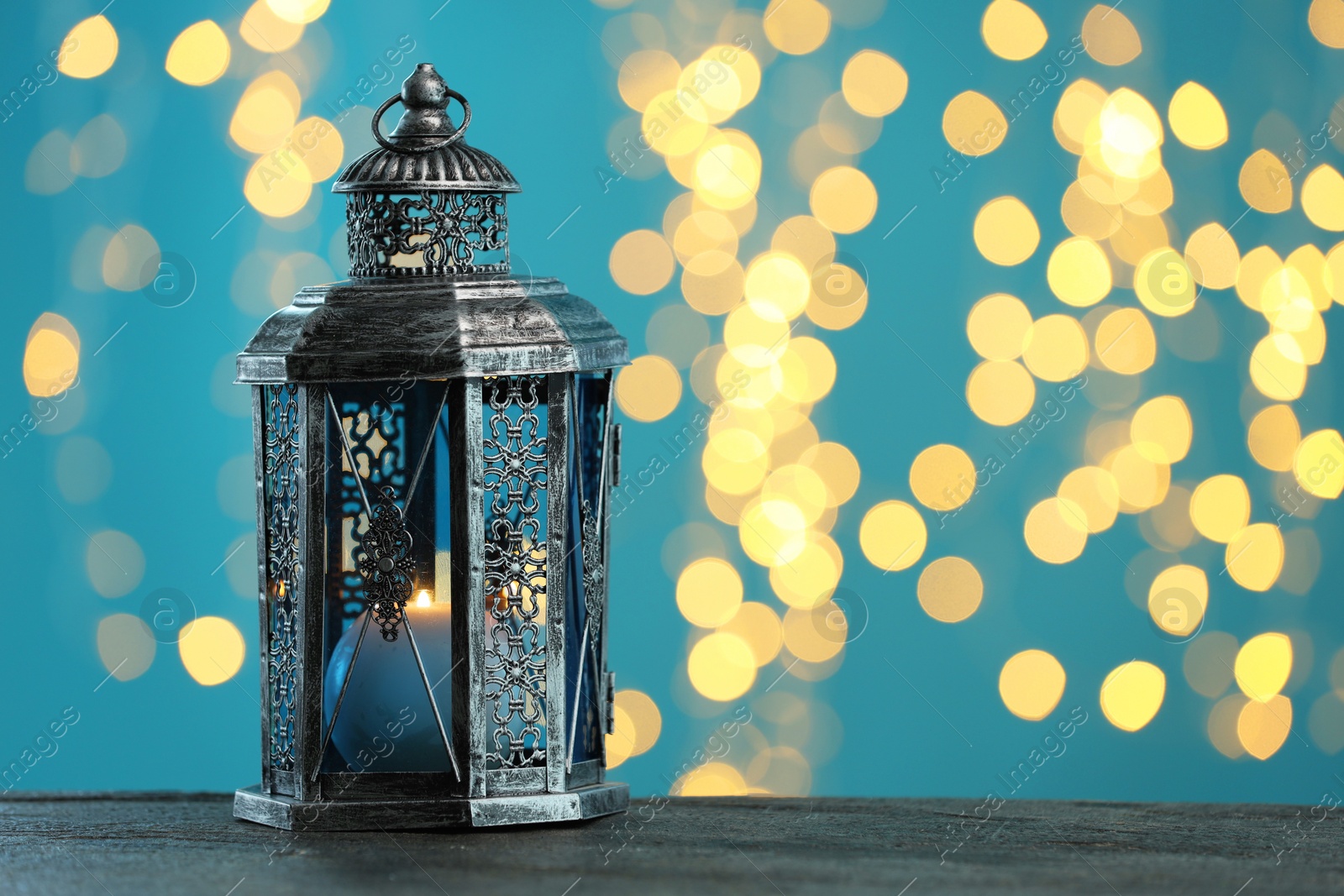 Photo of Traditional Arabic lantern on wooden table against light blue background with blurred lights. Space for text