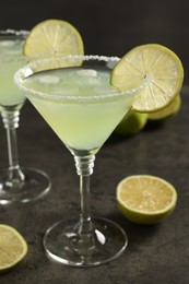 Delicious Margarita cocktail with ice cubes in glasses and lime on grey table