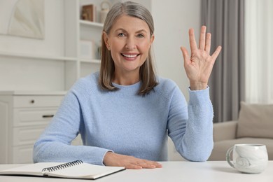 Photo of Happy woman waving hello at white table indoors