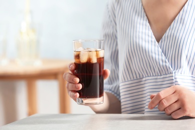 Photo of Woman with glass of cold cola at table indoors, closeup. Space for text