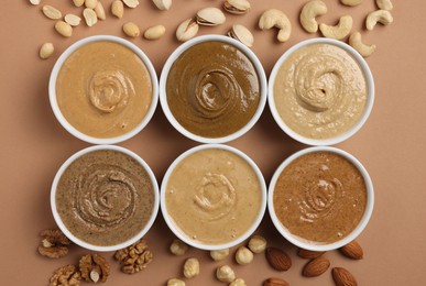 Many tasty nut butters in bowls and nuts on beige table, flat lay