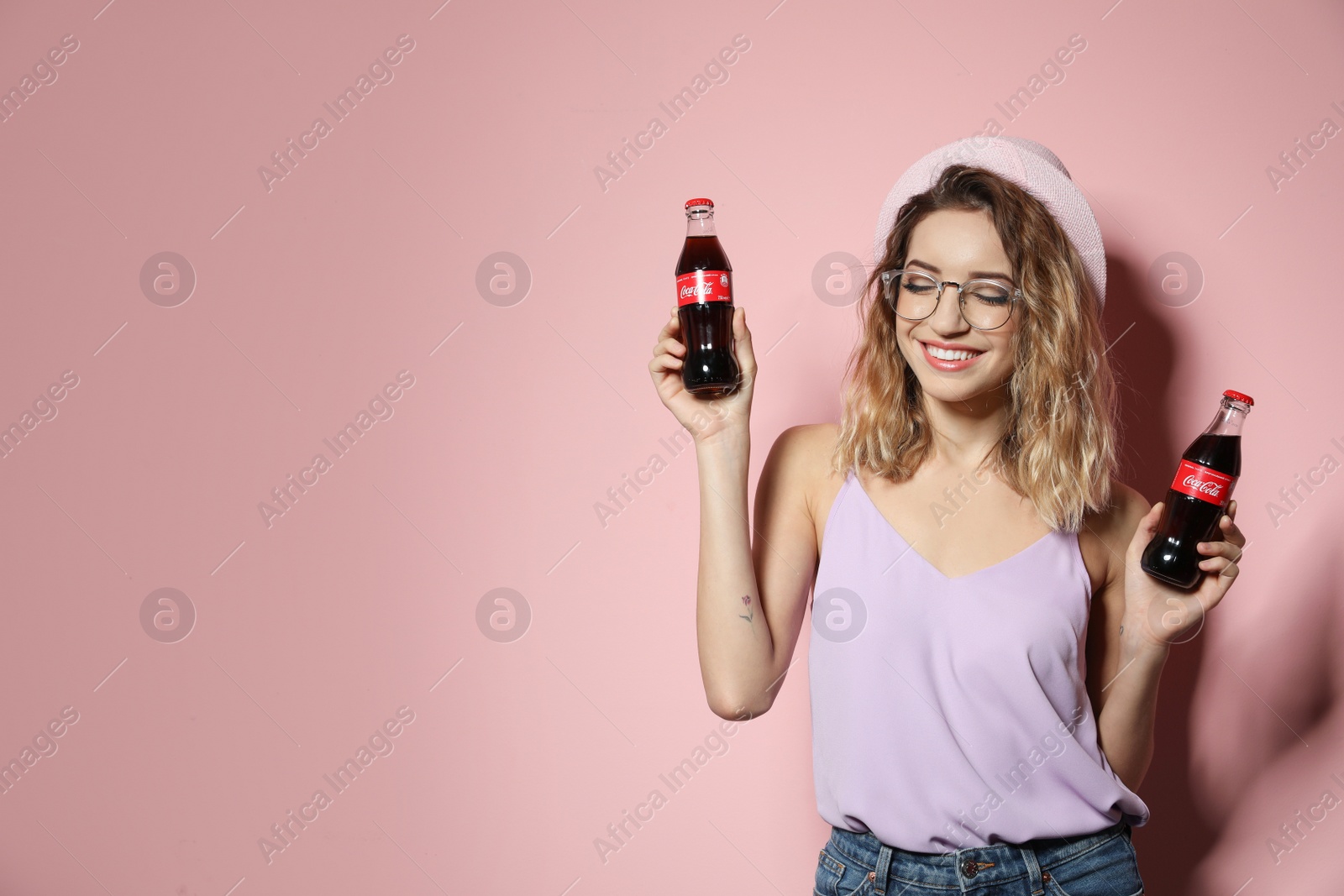 Photo of MYKOLAIV, UKRAINE - NOVEMBER 28, 2018: Young woman with bottles of Coca-Cola on color background, space for text