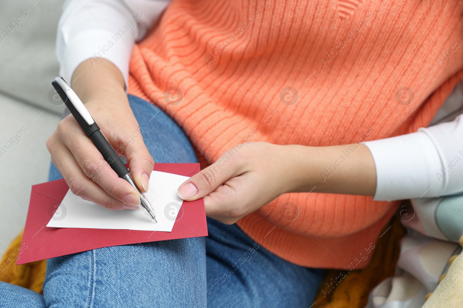 Photo of Young woman writing message in greeting card on sofa, closeup