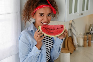 Photo of Beautiful young African American woman with slice of watermelon in kitchen at home