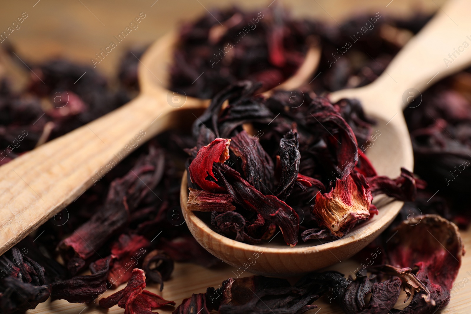 Photo of Wooden spoon with dry hibiscus tea on table, closeup