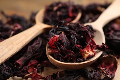 Wooden spoon with dry hibiscus tea on table, closeup