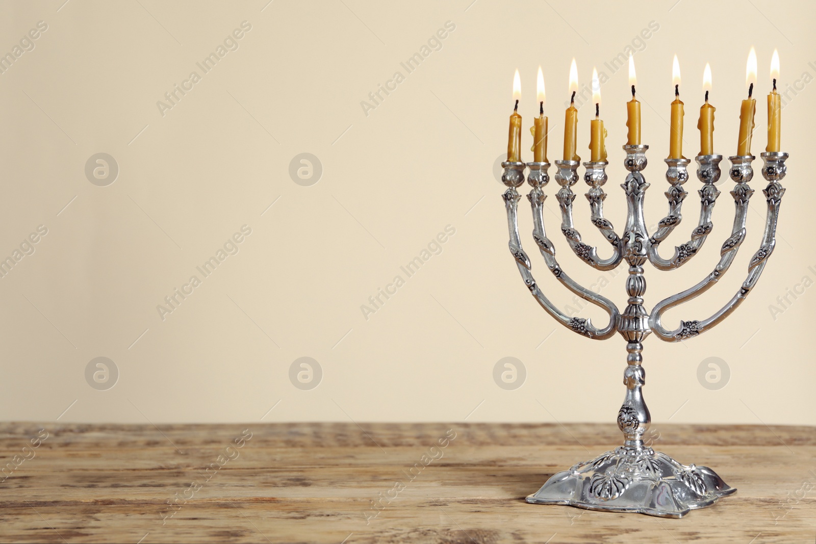 Photo of Silver menorah with burning candles on wooden table against beige background, space for text. Hanukkah celebration