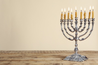 Silver menorah with burning candles on wooden table against beige background, space for text. Hanukkah celebration