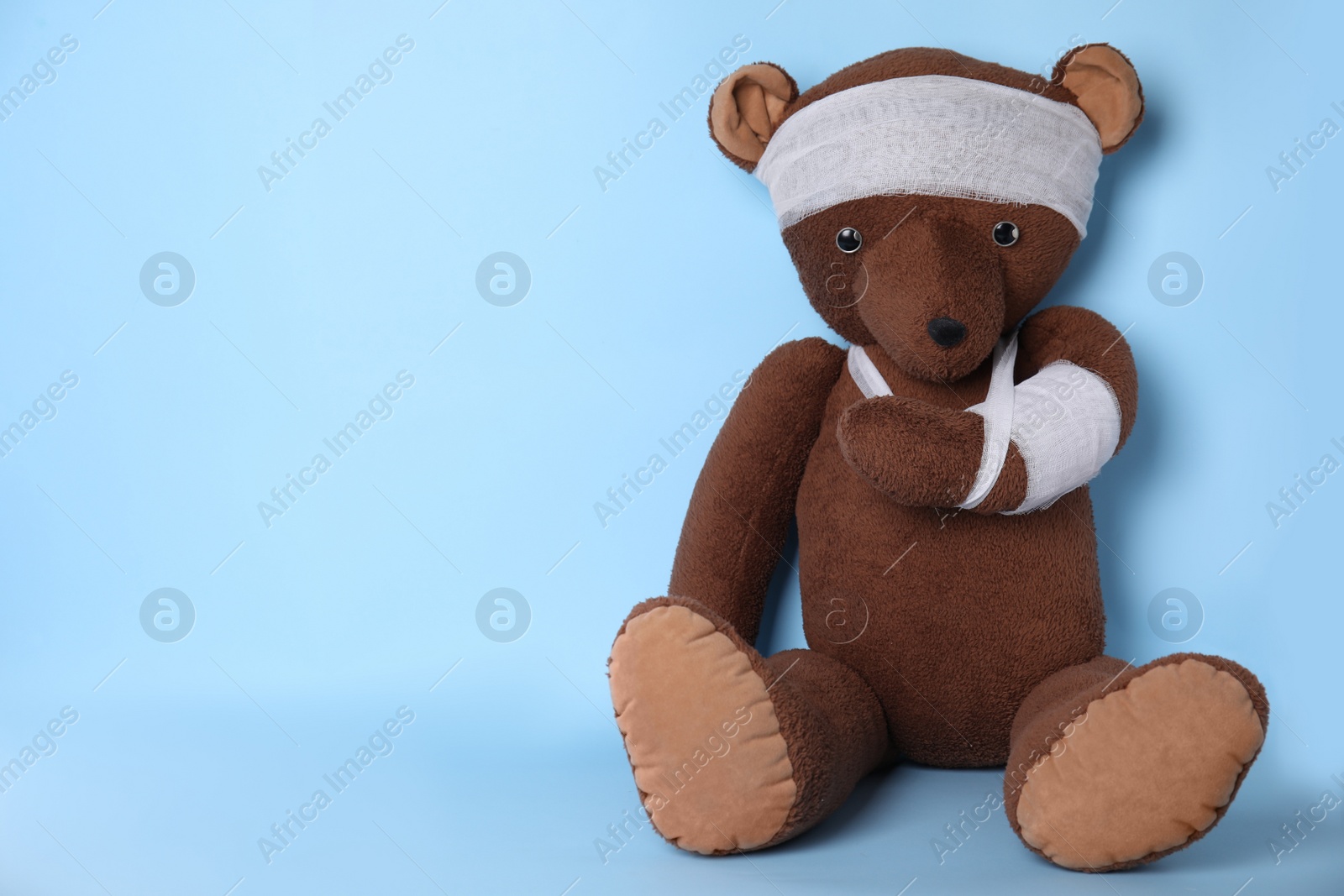 Photo of Toy bear with bandages on light blue background. Space for text