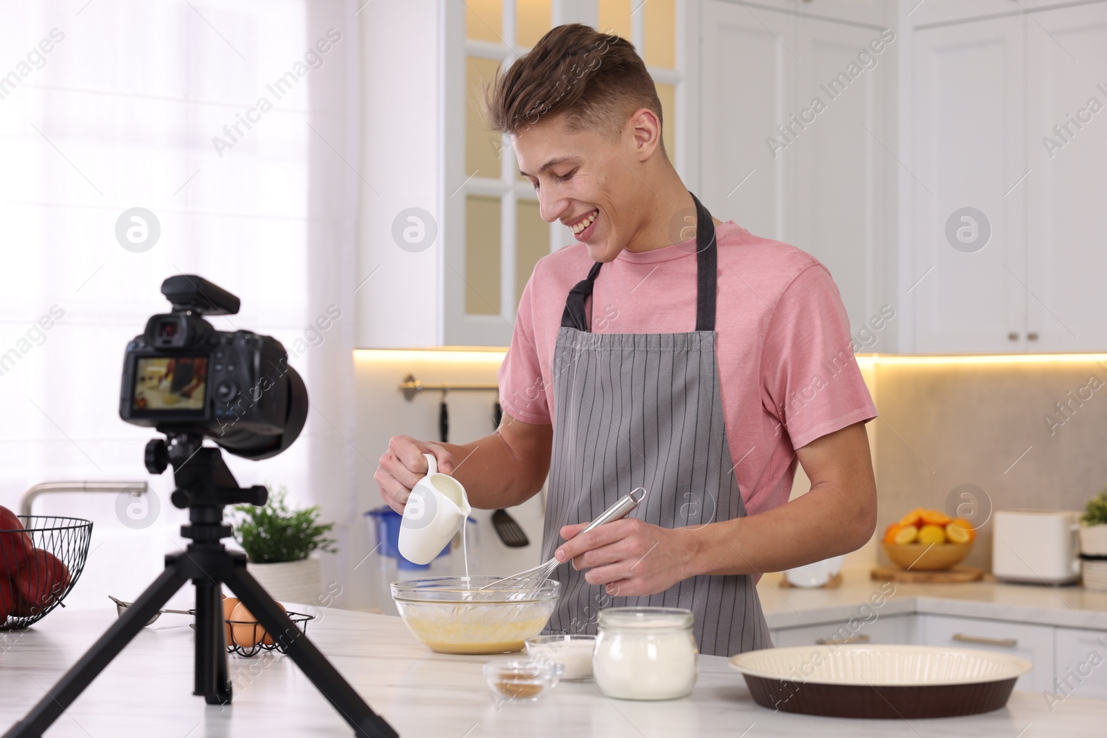 Photo of Smiling food blogger cooking while recording video in kitchen