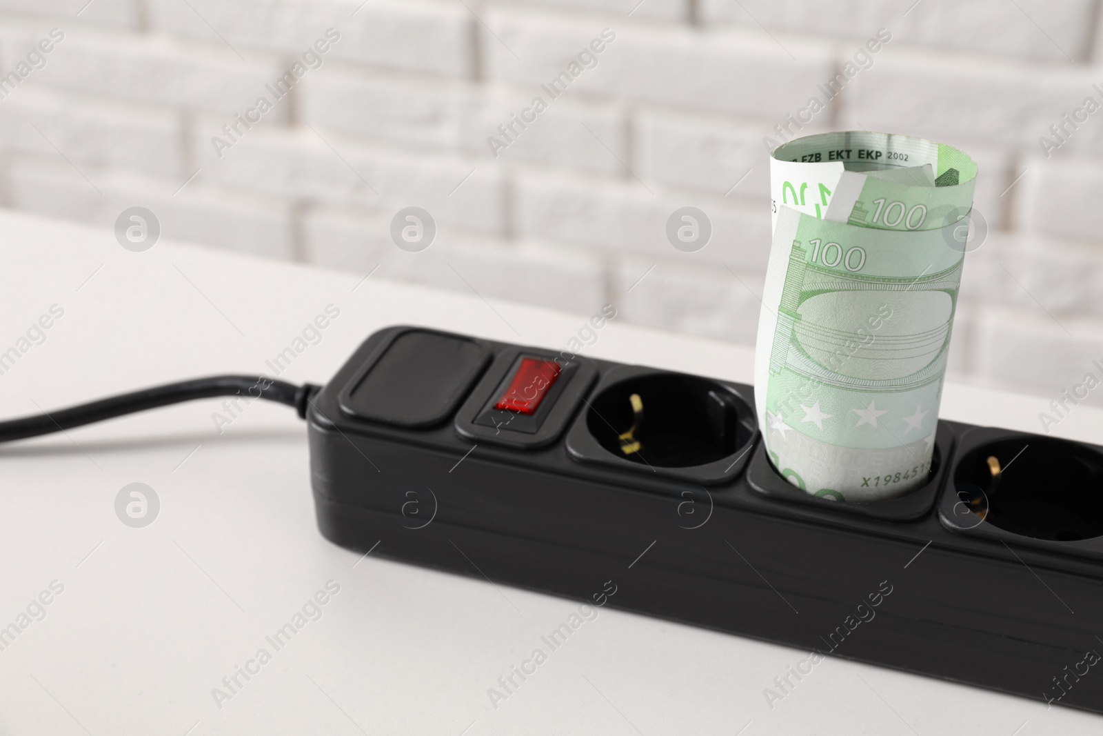 Photo of Extension board with rolled euro banknotes on white table near brick wall, closeup