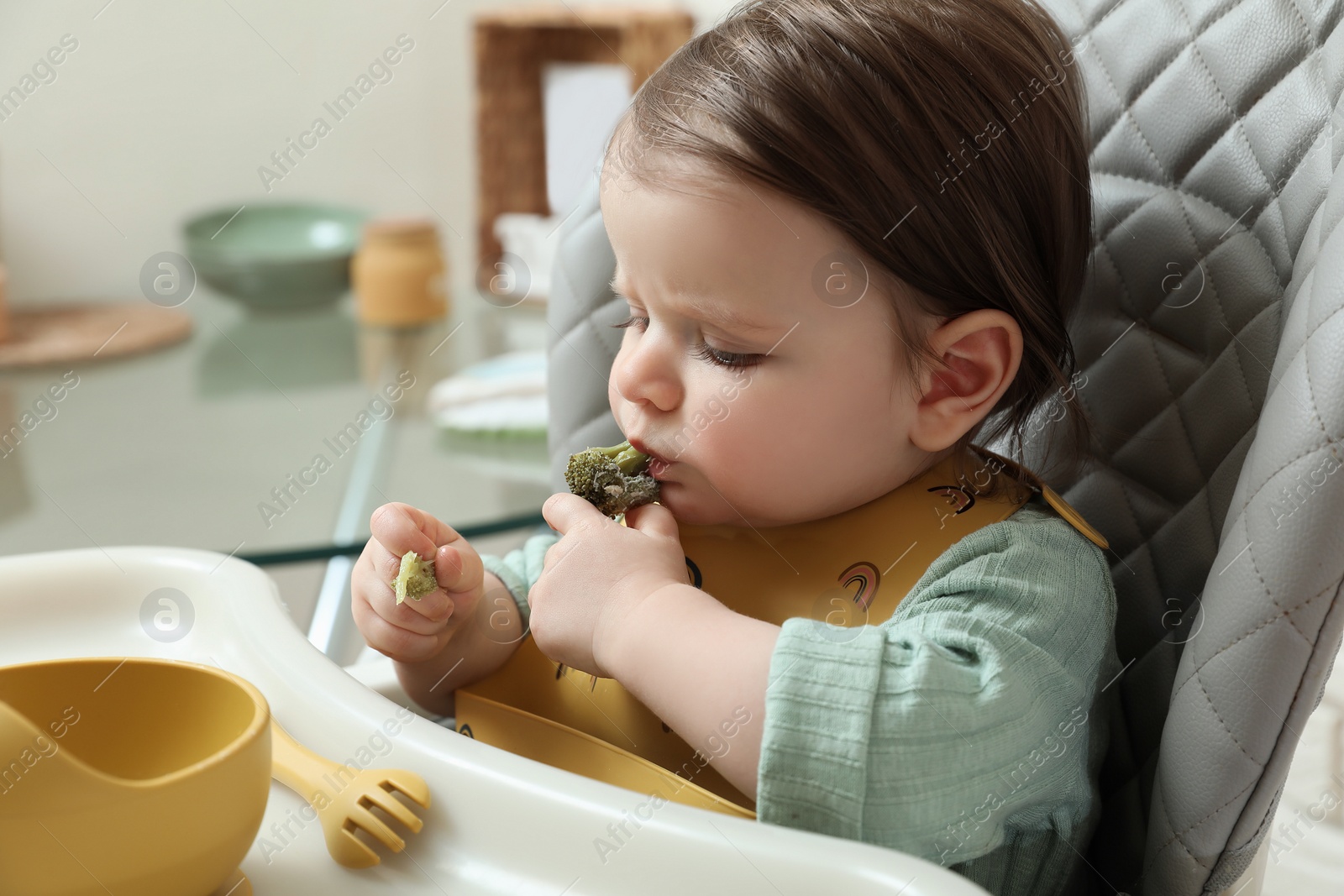 Photo of Cute little baby eating healthy food in high chair indoors