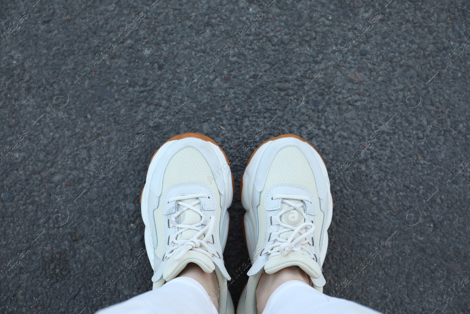 Photo of Woman in white sneakers standing on asphalt, top view