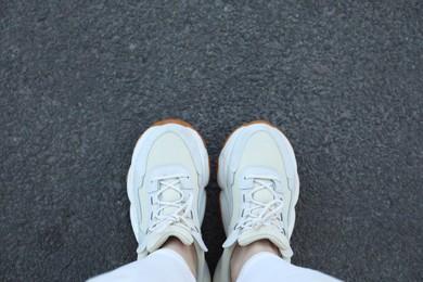 Photo of Woman in white sneakers standing on asphalt, top view