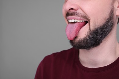 Photo of Happy man showing his tongue on light grey background, closeup. Space for text