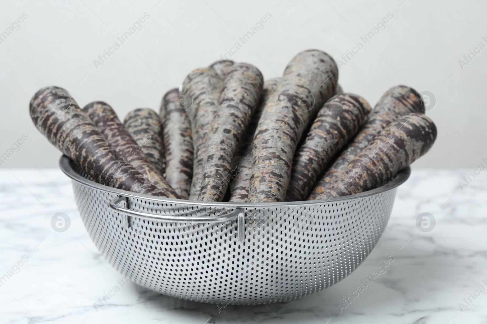 Photo of Raw black carrots in colander on white table