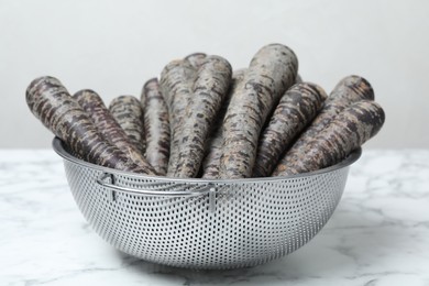 Raw black carrots in colander on white table