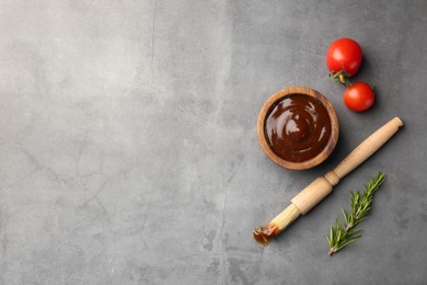 Photo of Tasty barbeque sauce in bowl, tomato, rosemary and brush on grey textured table, flat lay. Space for text