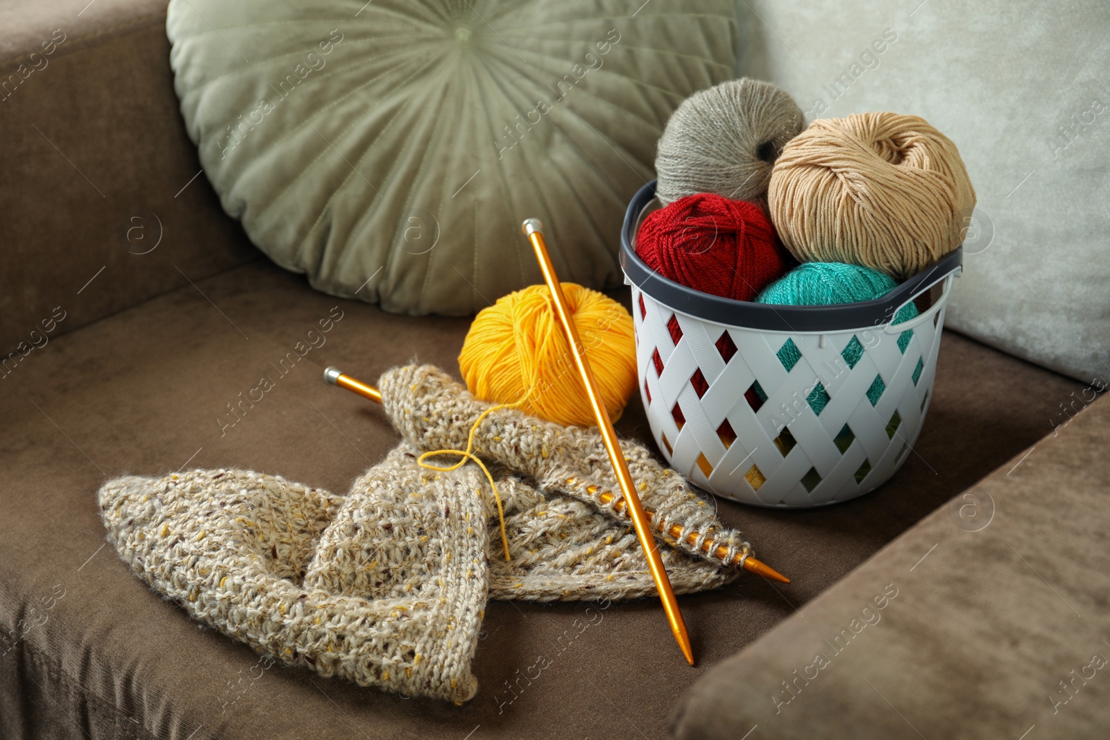 Photo of Soft woolen yarns, knitting and needles on brown sofa