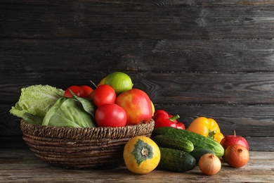 Photo of Basket with fresh fruits and vegetables on wooden table, space for text
