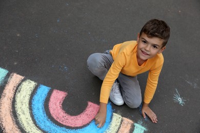 Happy child drawing rainbow with chalk on asphalt, above view