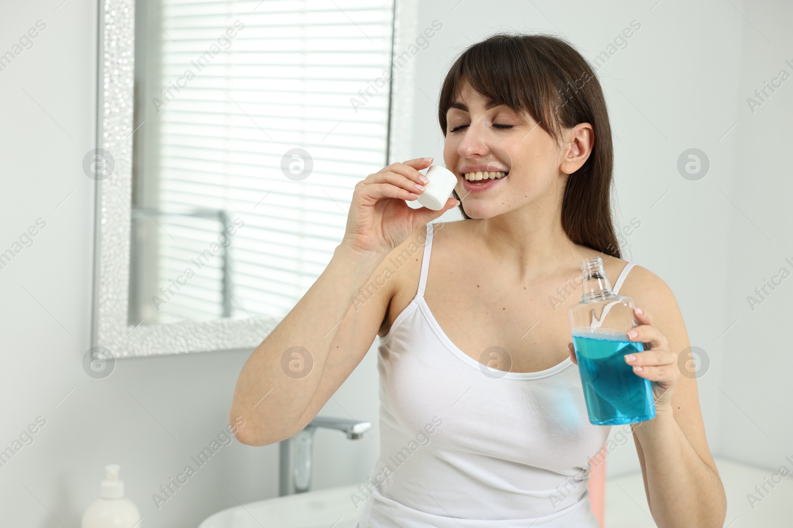 Photo of Young woman using mouthwash in bathroom. Oral hygiene