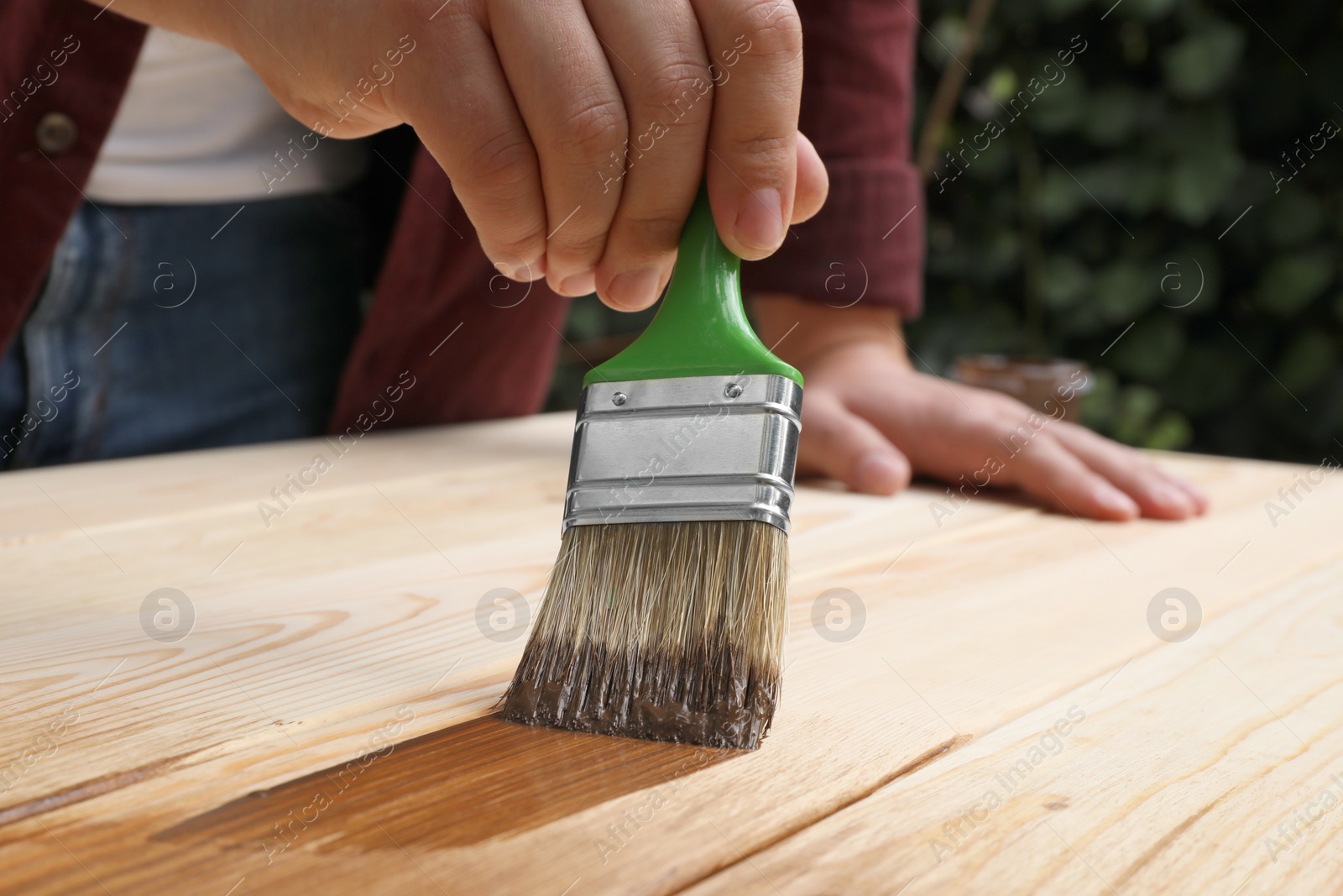 Photo of Man applying wood stain onto wooden surface against blurred background, closeup