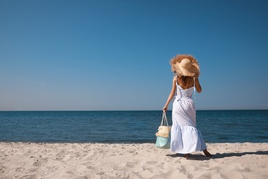 Photo of Woman with beach bag and straw hat on sand near sea, back view