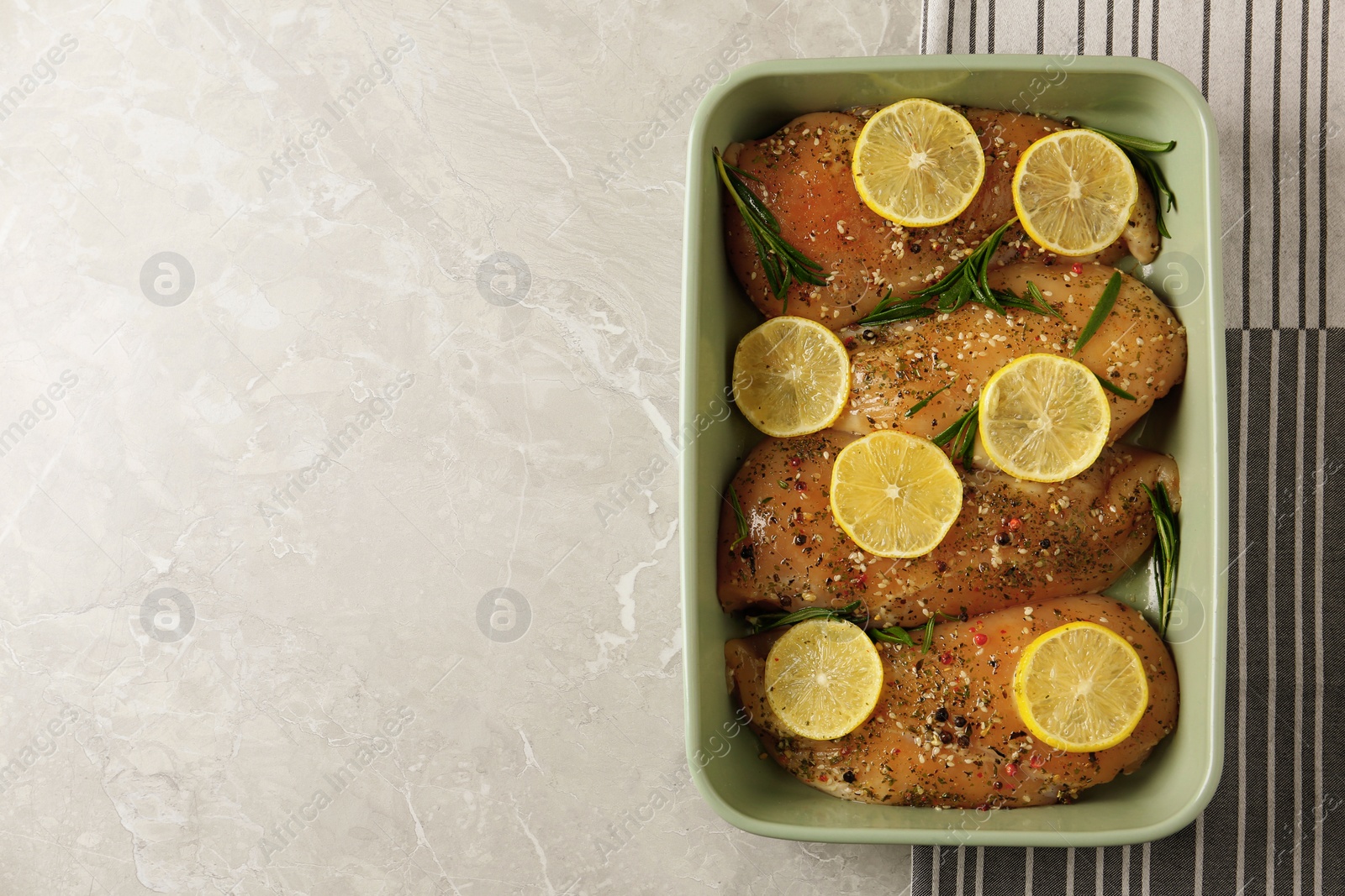 Photo of Chicken breasts with lemon and rosemary on grey table, top view. Space for text