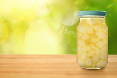 Jar of pickled onion bulbs on wooden table against blurred background, space for text