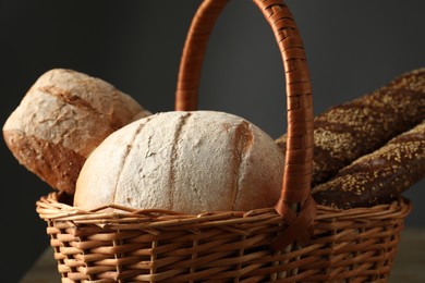 Wicker basket with different types of fresh bread on table, closeup