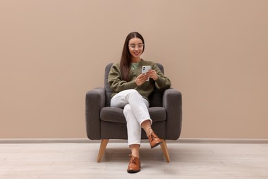Photo of Beautiful woman with smartphone sitting in armchair near beige wall indoors