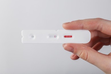 Photo of Woman holding disposable Covid-19 express test on light background, closeup