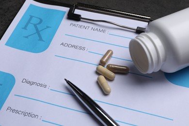 Medical prescription form, pills, bottle and pen on dark grey table, closeup