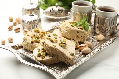 Photo of Tasty halva with pistachios and mint served on white table, closeup