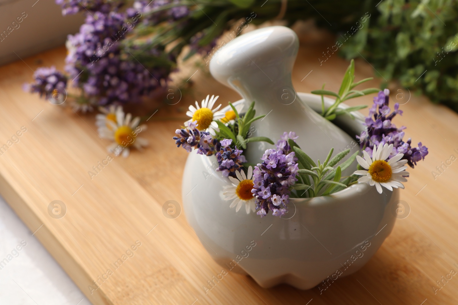 Photo of Mortar with fresh lavender, chamomile flowers, rosemary and pestle on wooden table, space for text