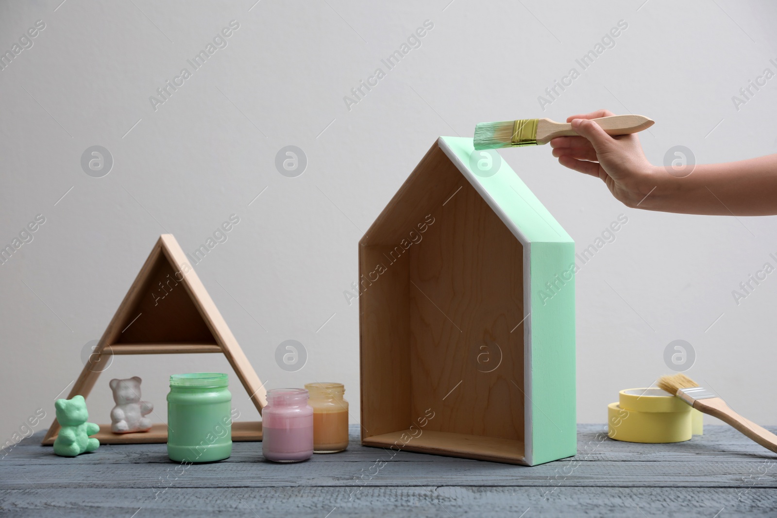 Photo of Woman painting wooden house model at grey table, closeup