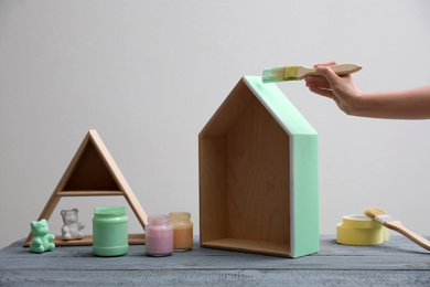 Photo of Woman painting wooden house model at grey table, closeup