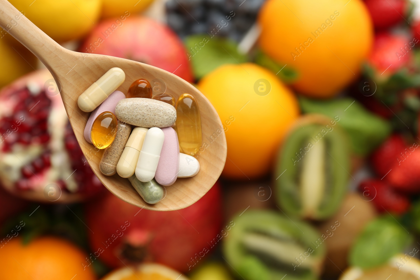 Photo of Different vitamin pills in spoon over fresh fruits, top view. Space for text