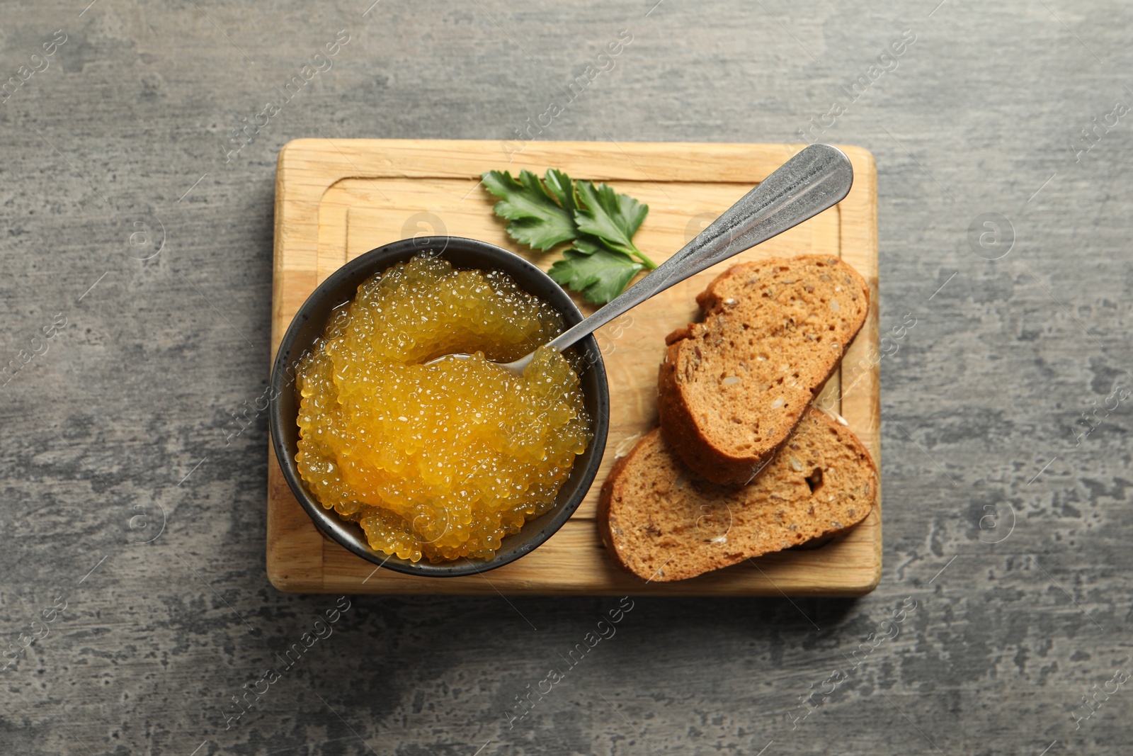 Photo of Fresh pike caviar in bowl, parsley and bread on grey table, top view