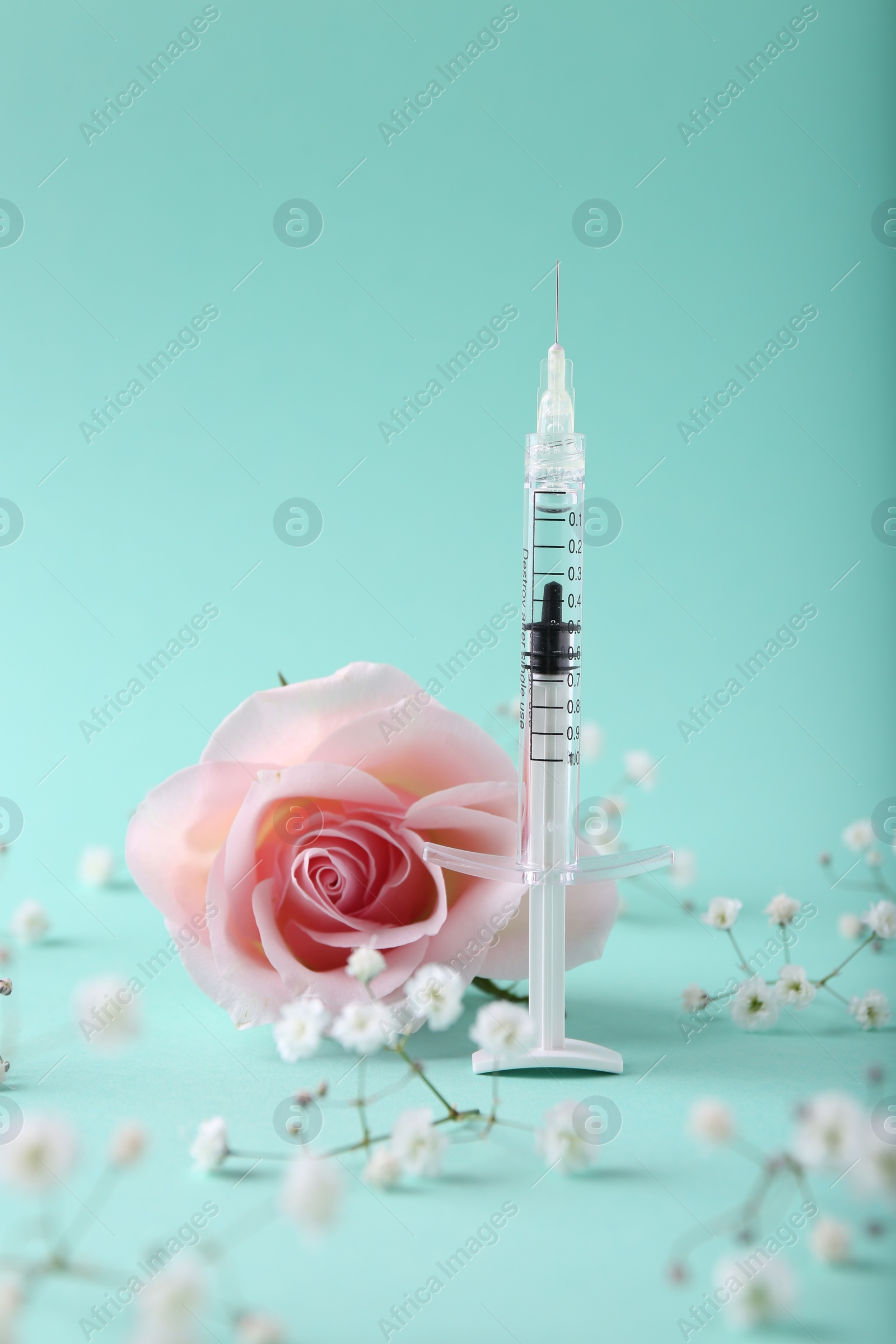 Photo of Cosmetology. Medical syringe, rose and gypsophila flowers on turquoise background