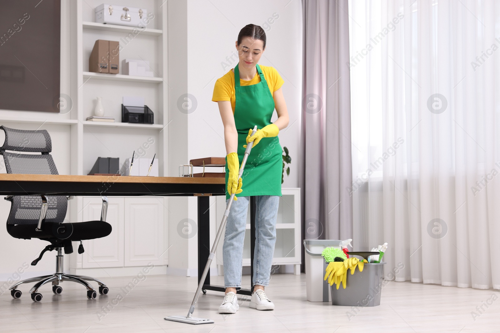 Photo of Cleaning service worker washing floor with mop. Bucket with supplies in office