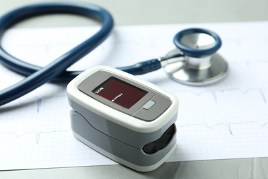 Modern fingertip pulse oximeter, stethoscope and cardiogram on grey table, closeup
