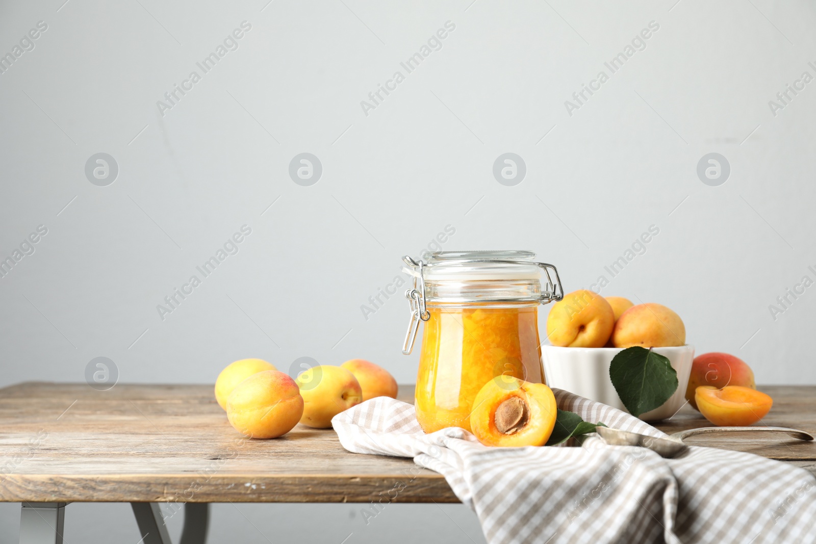 Photo of Jar of apricot jam and fresh fruits on wooden table. Space for text