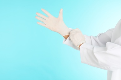 Male doctor putting on rubber gloves against color background, closeup with space for text. Medical object