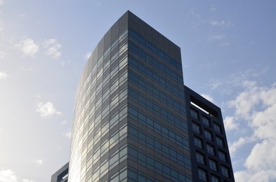 Exterior of beautiful modern skyscraper against blue sky, low angle view