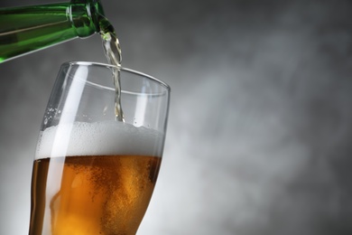 Pouring cold tasty beer from bottle into glass on grey background, closeup. Space for text