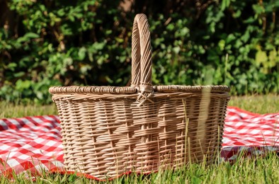 Photo of Picnic basket with checkered tablecloth on green grass outdoors