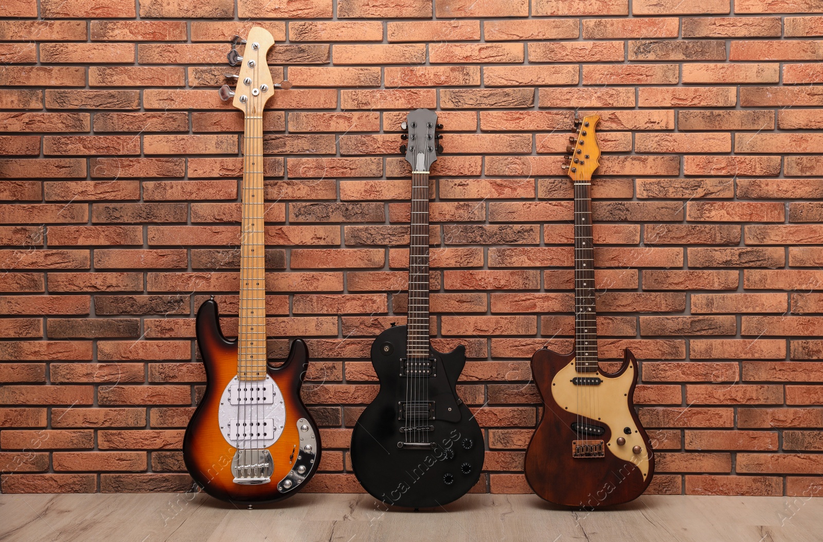 Photo of Modern electric guitars near red brick wall indoors. Band practice